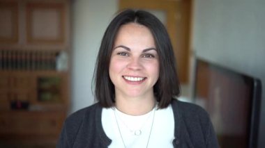 Beyaz tişörtlü, gülümseyen güzel kız arka planı bulanık odada duruyor..