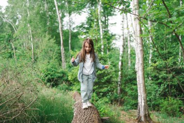 Ağaç gövdesinde dengede duran rahat elbiseli bir çocuk. Kavram: eğlenceli keşif, doğal merak, erken bağımsızlık, hareketin keyfi