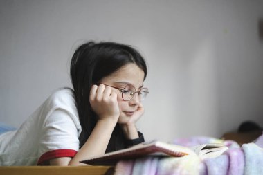 Gözlüklü bir genç odasında huzur içinde kitap okuyor. Konsept: öz düşünme, öğrenme, rahatlık, gençlik rutini, sakin bir akşam