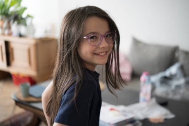 Dağınık bir yatak odasında gözlük takan mutlu bir kız. Kavram: doğal anlar, rahat atmosfer, çocukluk spontanlığı, gerçek mutluluk.