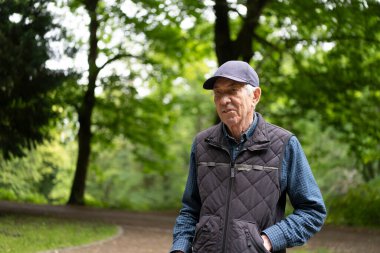 Beyzbol şapkalı, yorgun, yaşlı bir adam parkta yürüyor. Konsept: Yaşlanma zorlukları, esneklik, günlük yaşam, insan hassasiyeti, sessiz sebat