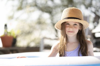 Güneşli bir günde küçük bir havuzda serinleyen gülen kız. Kavram: ferahlatıcı anlar, çocukluk sevinci, ısı çıkışı, evde eğlence.