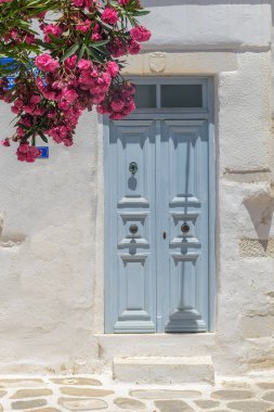 Typical Cycladitic architecture of a whitewashed facade of a house  with a typical traditional door and  blooming flowers in Parikia, Paros island, Greece.