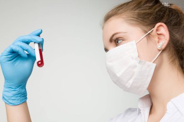 Tıbbi maskeli ve tıbbi eldivenli genç bir kadın laboratuarda bir kan sondasıyla ilgileniyor.