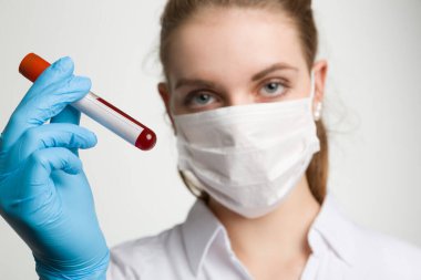 Tıbbi maskeli ve tıbbi eldivenli genç bir kadın laboratuarda bir kan sondasıyla ilgileniyor.