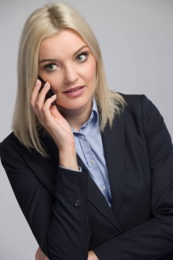 İş elbiseli genç sarışın kadın cep telefonu kullanıyor ve dinliyor.