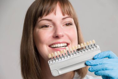 Diş hekiminin yakın çekimi, dişlerin beyazlatılması ya da yeni takma dişler için kaplamasını kontrol etmek için kadının ağzındaki gölge rehberini kullanıyor.