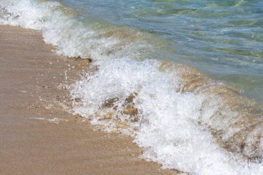 Güneşli bir günde, dalgalar kumsalda sörf yapar.