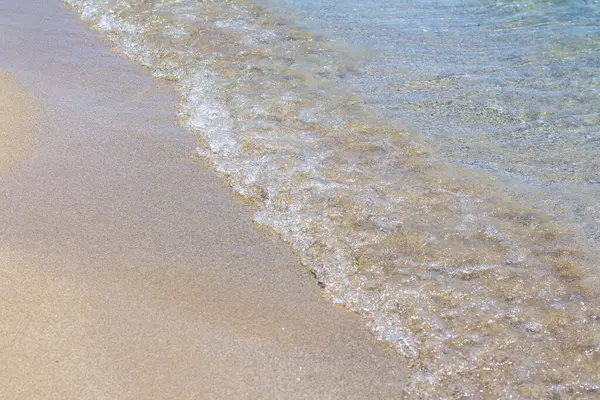 Güneşli bir günde, dalgalar kumsalda sörf yapar.