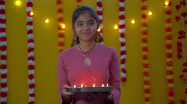 Diwali Hindu Işık Festivali. Sarı arka planı olan kadınların ellerinde Diya ya da yağ lambası. Geleneksel kıyafetler giyen güzel Hintli kızın portresi.