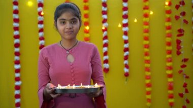Diwali Kutlaması için elinde diya ya da gaz lambası tutan şirin Hintli genç kız. Diwali Hindu Işık Festivali. Sarı arka planı olan kadınların ellerinde Diya ya da yağ lambası. Geleneksel kıyafetler giyen güzel Hintli kızın portresi.