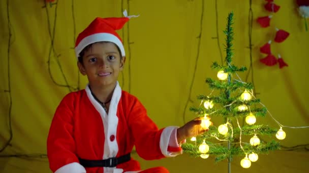 黄色の背景に贈り物と赤いクリスマスの衣装のアジアの小さな男の子 クリスマスのサンタの帽子で満足の小さな子供の少年の肖像画 黄色の背景に隔離された笑い — ストック動画