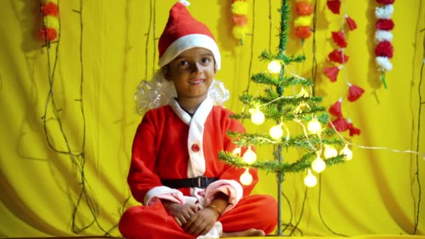 黄色の背景に贈り物と赤いクリスマスの衣装のアジアの小さな男の子 クリスマスのサンタの帽子で満足の小さな子供の少年の肖像画 黄色の背景に隔離された笑い — ストック動画