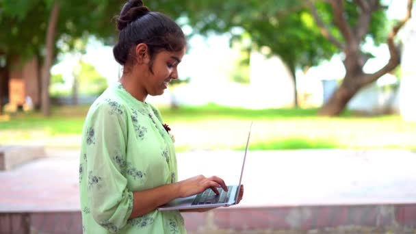 ラップトップコンピュータを使用して笑顔のインドの十代の少女の肖像画 青いスタジオの背景でオンラインで勉強 コピースペース付きのバナーデザイン — ストック動画