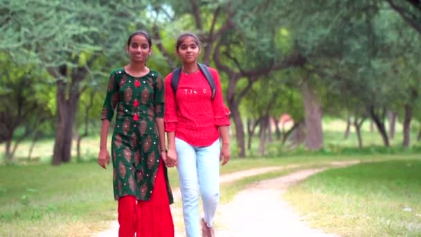 陽気な女の子のフルサイズの写真は 学校にバックパックの教育を着用します 公園で一緒に歩いている二人の友人 — ストック動画