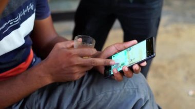 Genç adam yerel çay dükkanında çay içer. Adam çay içiyor ve boş zamanlarında akıllı telefondan video izliyor. Sikar, Rajasthan, Hindistan - Kasım 2022