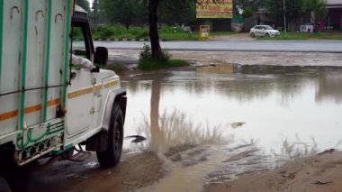 Yağmur sezonu boyunca asfaltsız ve çamurlu yol. Kötü yola saplanmış bir araç kazaya sebep oluyor. Rajasthan, Hindistan - Kasım 2022