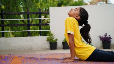 Küçük tatlı kız yoga yapıyor. Paspasın üstünde duruyor.. 