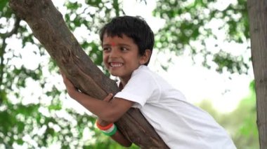 Beyaz tişörtlü küçük çocuk ağaç parkında oynuyor ve tırmanıyor.