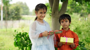 Küçük şirin Hintli kız kardeş Rakhi 'yi küçük kardeşinin bileğine bağlıyor ve Raksha Bandhan ya da Bhai Dooj festivalinde hediye ve tatlı değiş tokuşu yapıyor.