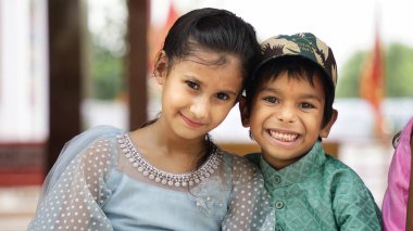 Rakhi 'yi küçük kardeşinin bileğine bağlayan ve Raksha Bandhan ya da Bhai Dooj festivalinde hediyelerini ve tatlılarını değiş tokuş eden tatlı Hintli kız kardeş beyaz arka planda izole bir şekilde oturuyor.