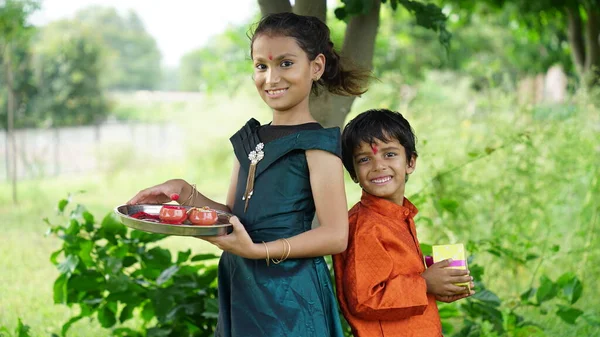Hindu Brother and sister in ethnic wear holding Indian sweets and gift boxes on the occasion of Raksha Bandhan festival
