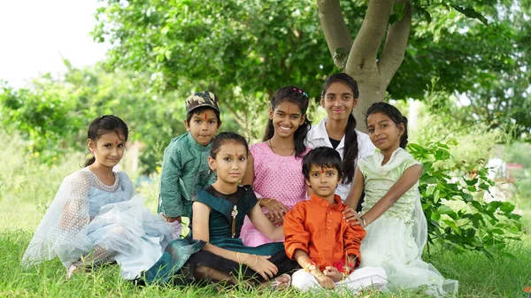 Indian brothers and sisters celebrating Raksha Bandhan or Rakhi festival at garden while wearing traditional cloths and sitting over nature background