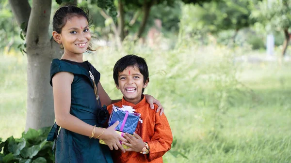 Hindu Brother and sister in ethnic wear holding Indian sweets and gift box on the occasion of Raksha Bandhan festival