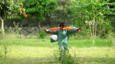 Arkadaki yeşillikte Hindistan bayrağıyla koşan şirin küçük Hintli çocuk Bağımsızlık Günü 'nü ya da Hindistan Cumhuriyeti' ni kutluyor.