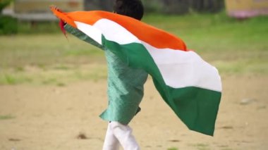 Arkadaki yeşillikte Hindistan bayrağıyla koşan şirin küçük Hintli çocuk Bağımsızlık Günü 'nü ya da Hindistan Cumhuriyeti' ni kutluyor.