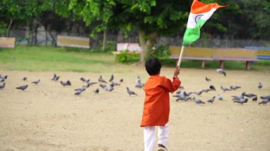 Arkadaki yeşillikte Hindistan bayrağıyla koşan şirin küçük Hintli çocuk Bağımsızlık Günü 'nü ya da Hindistan Cumhuriyeti' ni kutluyor.