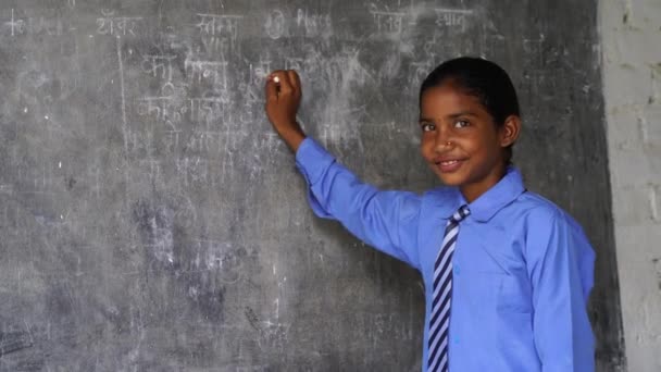 黒いチョークボードの背景の前に立っている幸せなインドの学校の少女の子供 教育コンセプトまたは学校に戻る — ストック動画