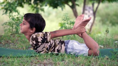 Dışarıda yoga yapan muhteşem bir çocuğun portresi. Güzel bir çocuk yoga yapıyor ya da jimnastik yapıyor. Nilüfer pozisyonunda meditasyon yapan küçük çocuklar