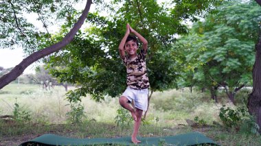 Dışarıda yoga yapan muhteşem bir çocuğun portresi. Güzel bir çocuk yoga yapıyor ya da jimnastik yapıyor. Nilüfer pozisyonunda meditasyon yapan küçük çocuklar