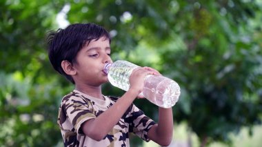 Çimenlerde oturan güzel bir çocuk yaz mevsiminde bir şişeden su içer. Oğlan sıcak bir günde susuzluğunu giderir.