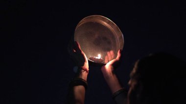 Karva Chauth, Hindu kadınların kocalarının güvenliği ve uzun ömürlülüğü için kutladıkları bir günlük festival. Hintli kadın, eleğe bakıyor, Karwa Chauth 'u kutluyor.