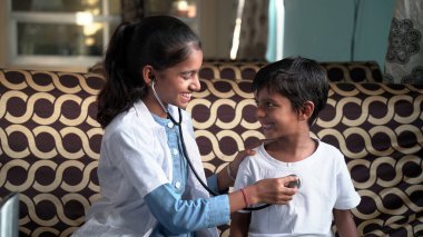 Mutlu çocuk gülümserken doktor güneşli ofiste sağlık kontrolü sırasında ciğerlerini ya da kalbini muayene ediyor. Genç hastasının kalp atışlarını ve solunumunu kontrol etmek için steteskop kullanan neşeli bir çocuk doktoru.