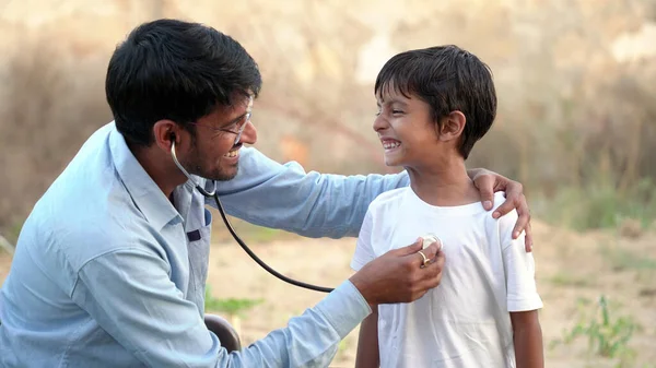 Indian village doctor of pediatrician holding stethoscope checking heartbeat of sick boy kid. health checkup, children medical insurance care. healthcare Concept