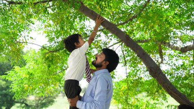 Yakışıklı babasının boynunda oturan ve gülümseyen sevimli oğlunun portresi doğa arka planında izole edilmiş.
