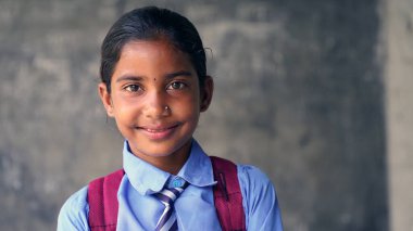 Sırt çantalı, kameraya bakan gülümseyen Hintli kırsal okul çocuğu. Gülümseyen bir okul üniforması giyen neşeli bir çocuk. İlkokul ve ilköğretim.