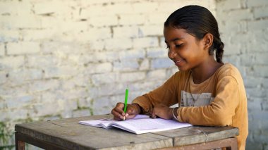 Sınıfta masa başında oturan mutlu Hintli okul çocuğunun portresi. Kalemleri ve defterleri olan okul öğrencileri. İlkokul, eğitim konsepti..