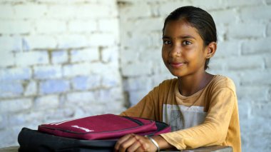 Sırt çantalı, kameraya bakan gülümseyen Hintli kırsal okul çocuğu. Gülümseyen bir okul üniforması giyen neşeli bir çocuk. İlkokul ve ilköğretim.