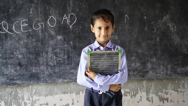 Happy Indian school girl child standing  in front of black chalkboard background. Education Concept or Back to School