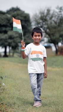 Mutlu Hindistan Sevimli Gülümseyen küçük çocuk dışarıda parka üç renkli bayrak sallayarak Bağımsızlık Günü 'nü veya Cumhuriyet Günü' nü kutluyor..