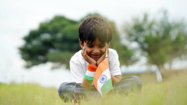 Mutlu Hindistan Sevimli Gülümseyen küçük çocuk dışarıda parka üç renkli bayrak sallayarak Bağımsızlık Günü 'nü veya Cumhuriyet Günü' nü kutluyor..