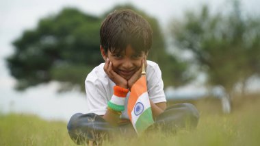 Beyaz ırktan yakışıklı küçük bir Hintli çocuk ya da çocuk Hindistan ulusal bayrağından ayakta duran ve vatanseverlik gösteren bir bebek giyer. Har Ghar Tiranga