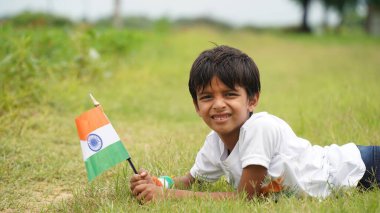 Mutlu Hindistan Sevimli Gülümseyen küçük çocuk dışarıda parka üç renkli bayrak sallayarak Bağımsızlık Günü 'nü veya Cumhuriyet Günü' nü kutluyor..