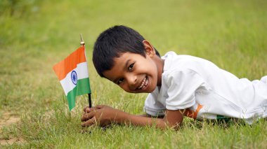 Beyaz ırktan yakışıklı küçük bir Hintli çocuk ya da çocuk Hindistan ulusal bayrağından ayakta duran ve vatanseverlik gösteren bir bebek giyer. Har Ghar Tiranga