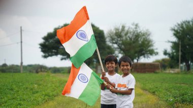 Mutlu Hindistan Sevimli Gülümseyen küçük çocuk dışarıda parka üç renkli bayrak sallayarak Bağımsızlık Günü 'nü veya Cumhuriyet Günü' nü kutluyor..