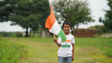 Beyaz ırktan yakışıklı küçük bir Hintli çocuk ya da çocuk Hindistan ulusal bayrağından ayakta duran ve vatanseverlik gösteren bir bebek giyer. Har Ghar Tiranga